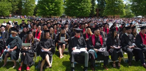 Faculty and students sit outside at commencement ceremony